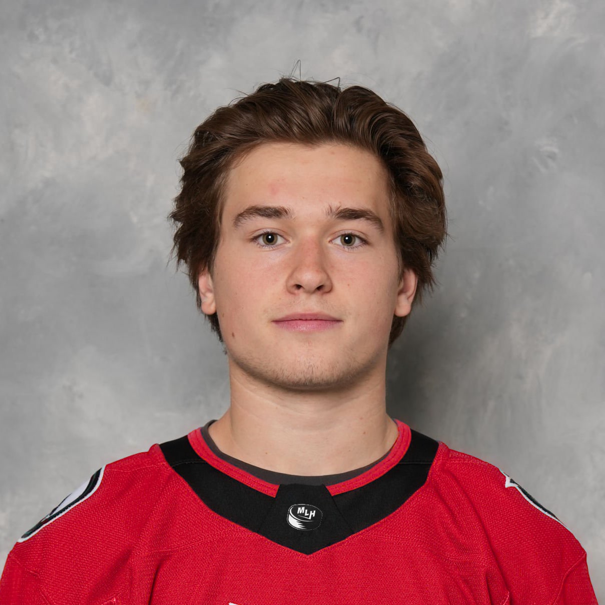 Photo of Luca Haas in a red jersey, with a generic grey photo studio backsplash behind him